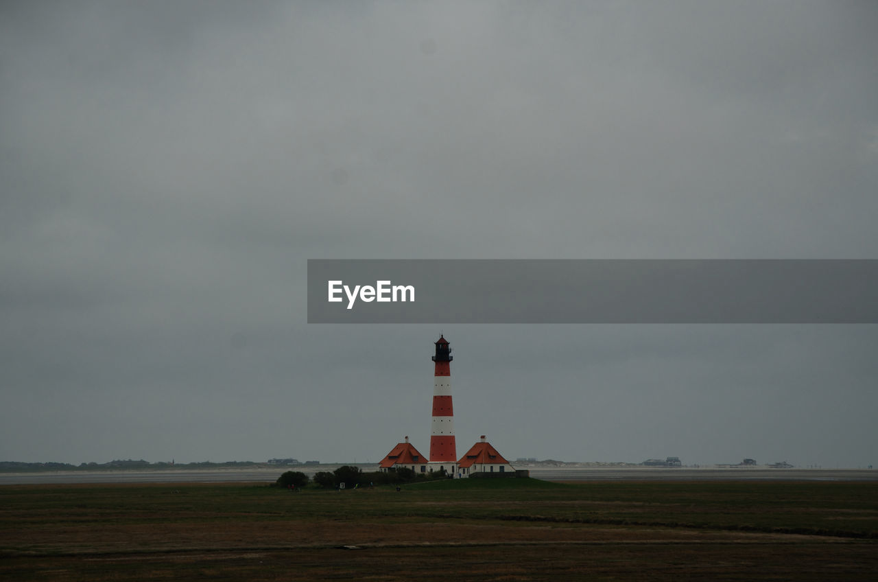 Lighthouse on field by building against sky