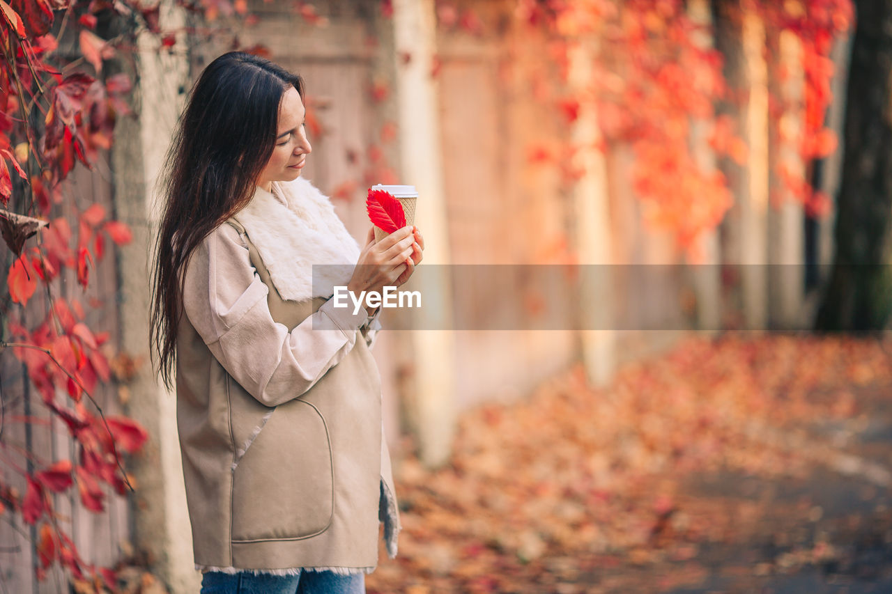 MIDSECTION OF WOMAN HOLDING UMBRELLA WHILE STANDING ON AUTUMN