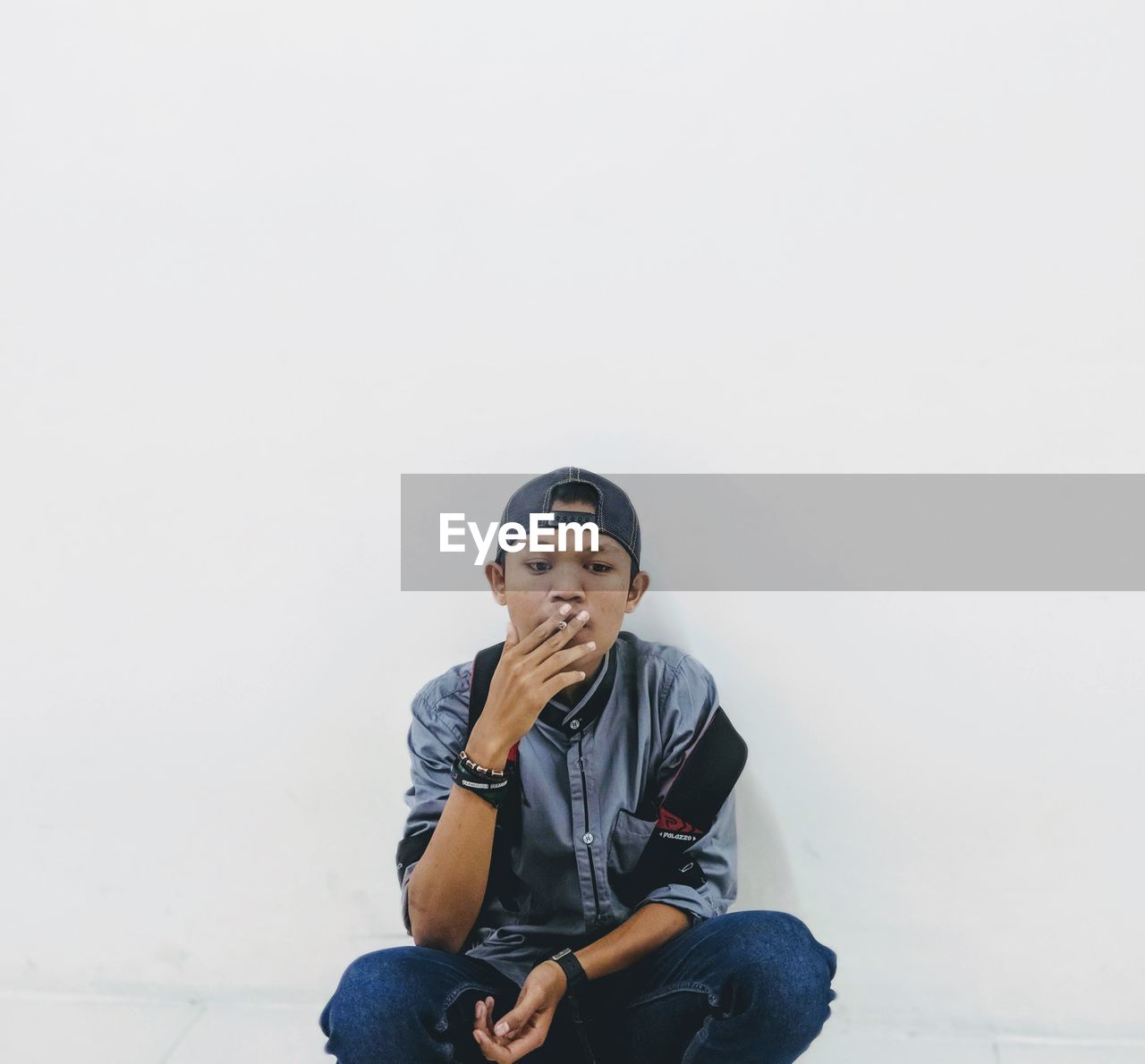 Portrait of smoker boy sitting against white wall 