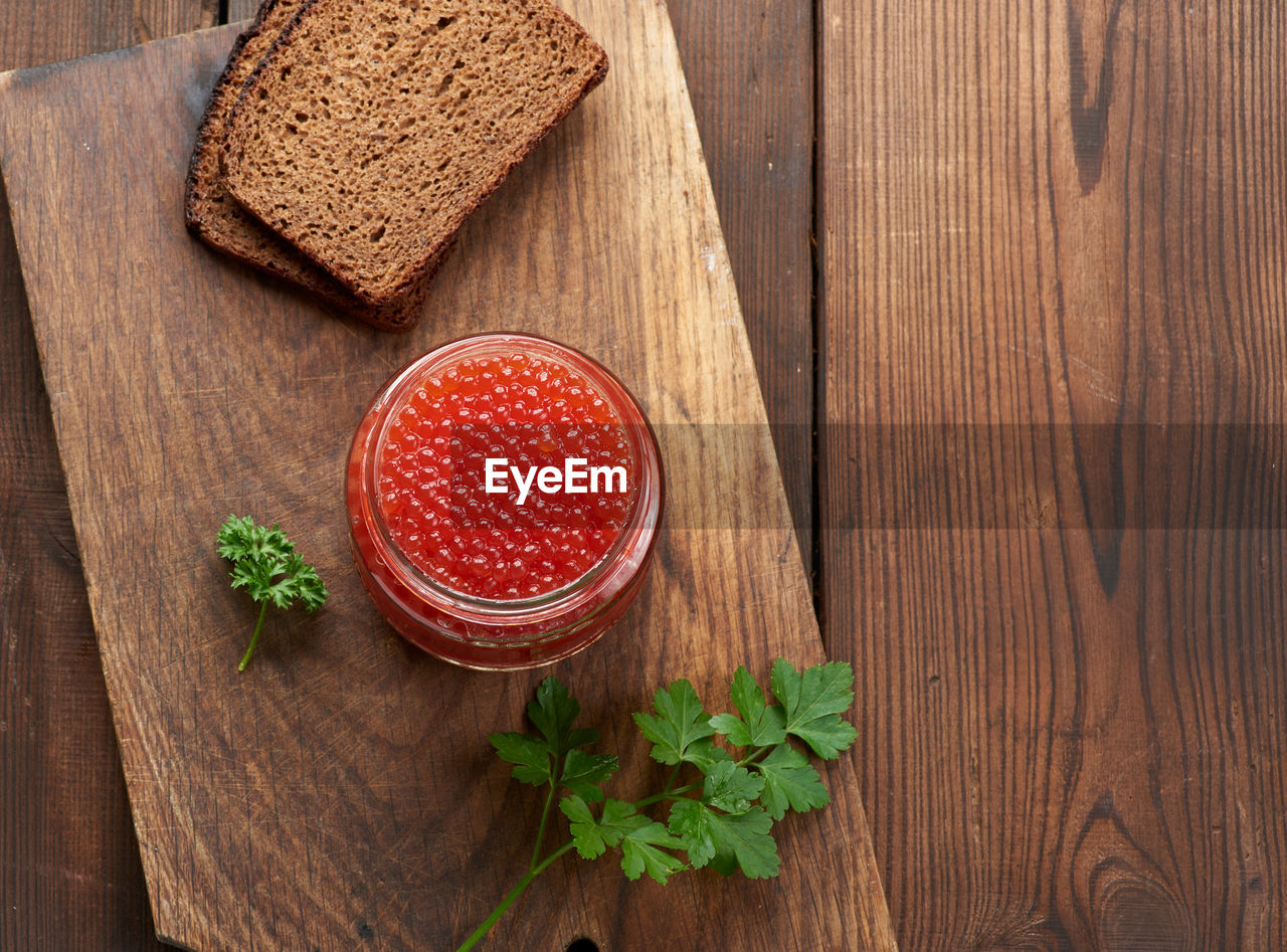 Full glass jar with red caviar on a brown wooden table, top view