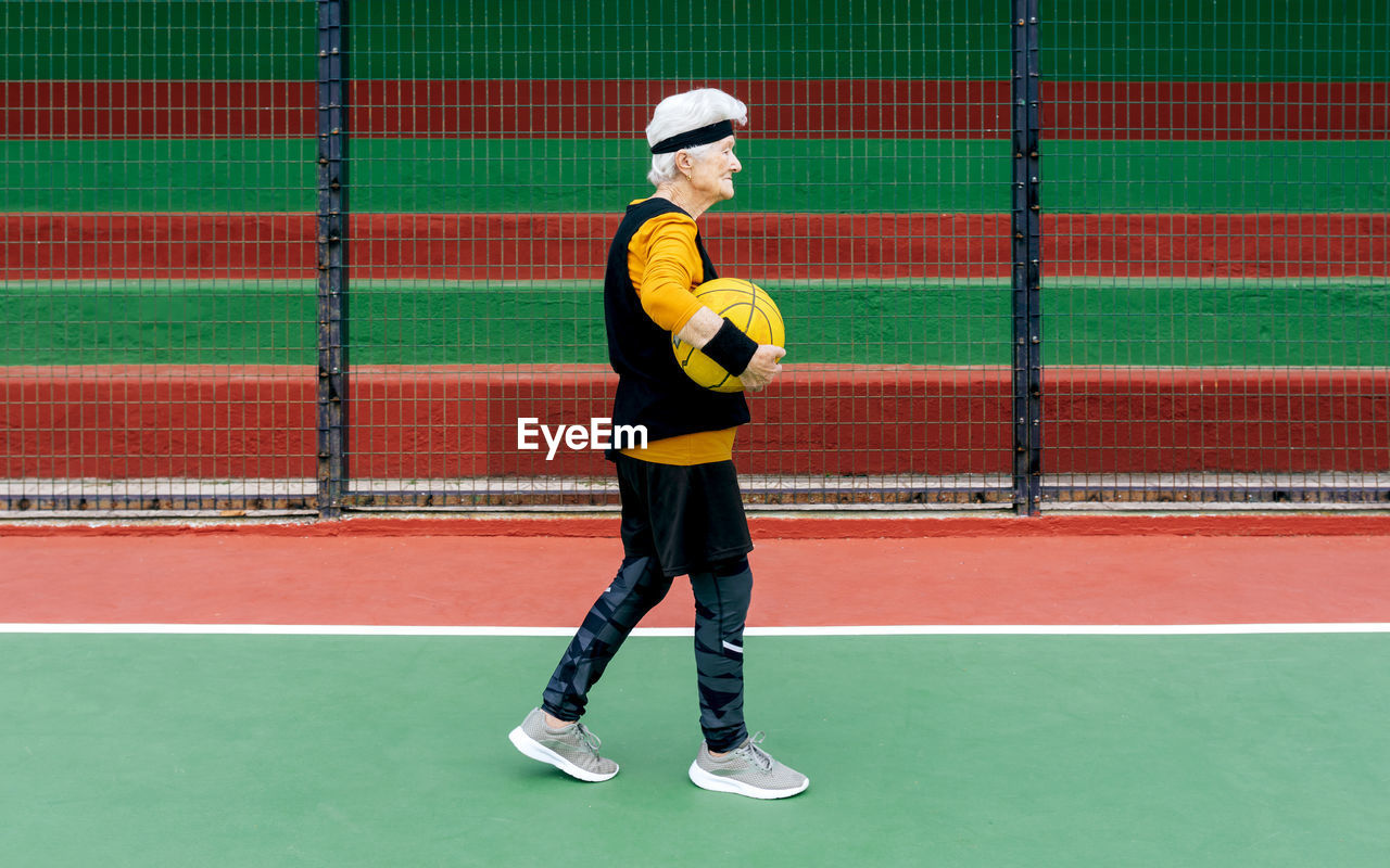 Side view mature female in activewear and headband looking away while walking with ball during basketball game