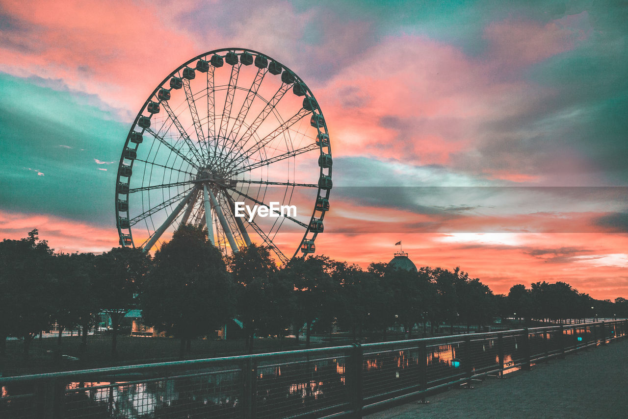 Ferris wheel against dramatic sky during sunset