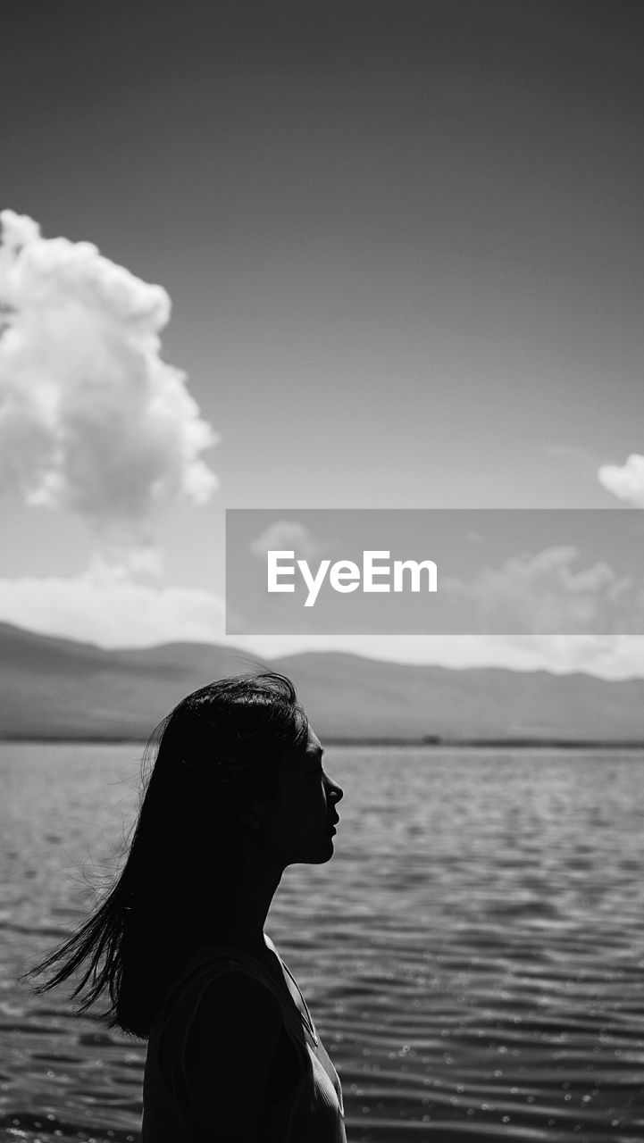 Side view of woman standing by sea against sky