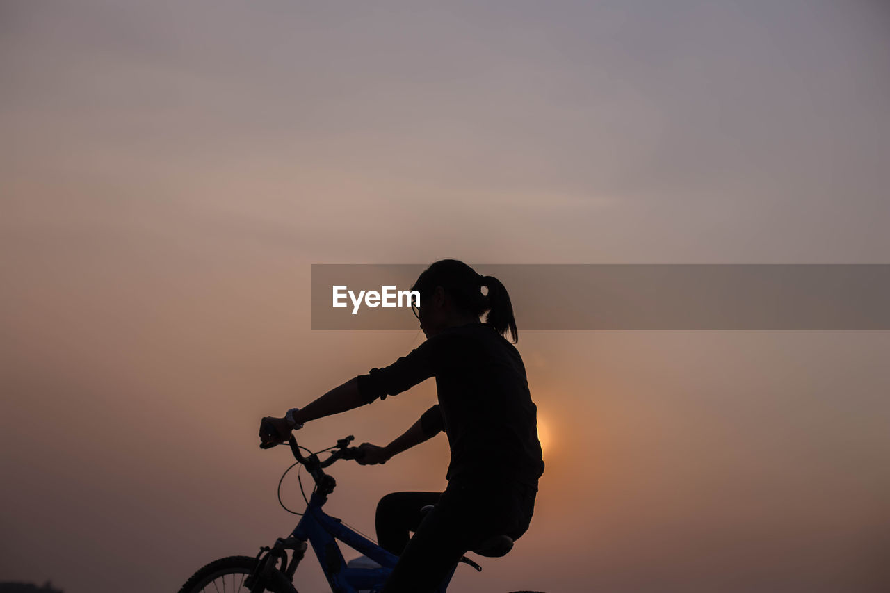 Silhouette woman riding bicycle against sky during sunset