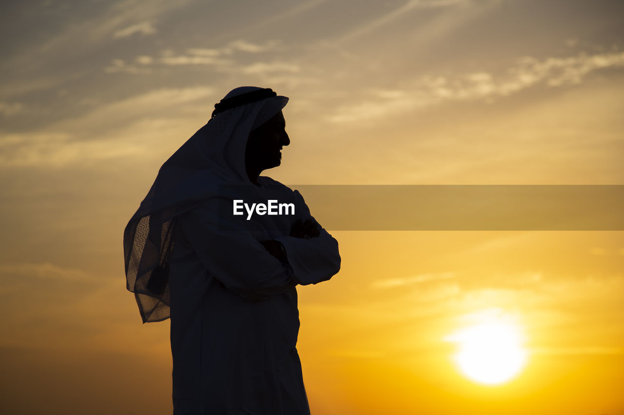 Side view of man in traditional clothing standing against sky during sunset
