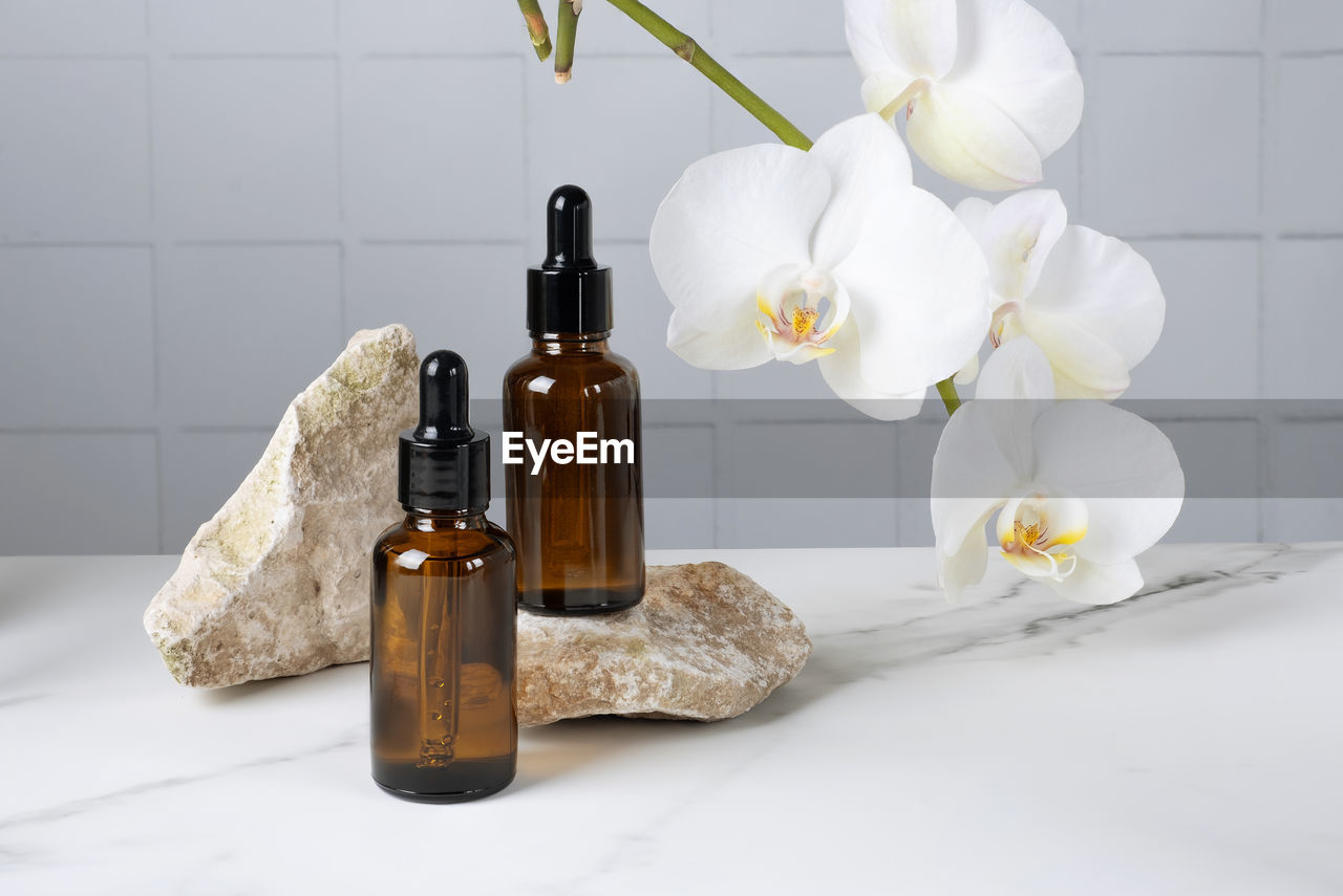 Bottles with pipette with cosmetic product for body skin care on stone against of a blooming orchid