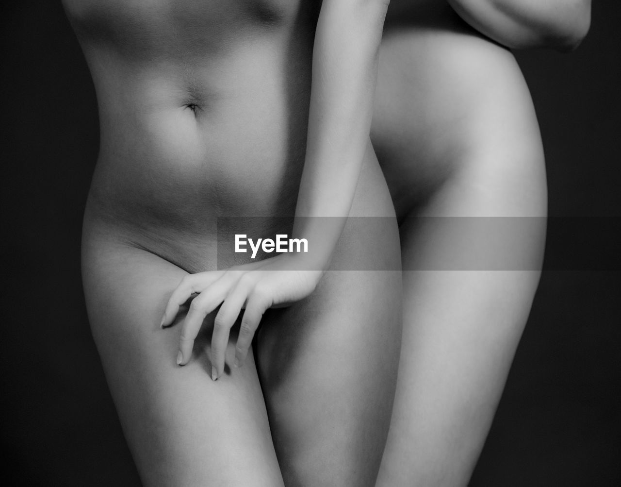 Midsection of naked women standing against black background