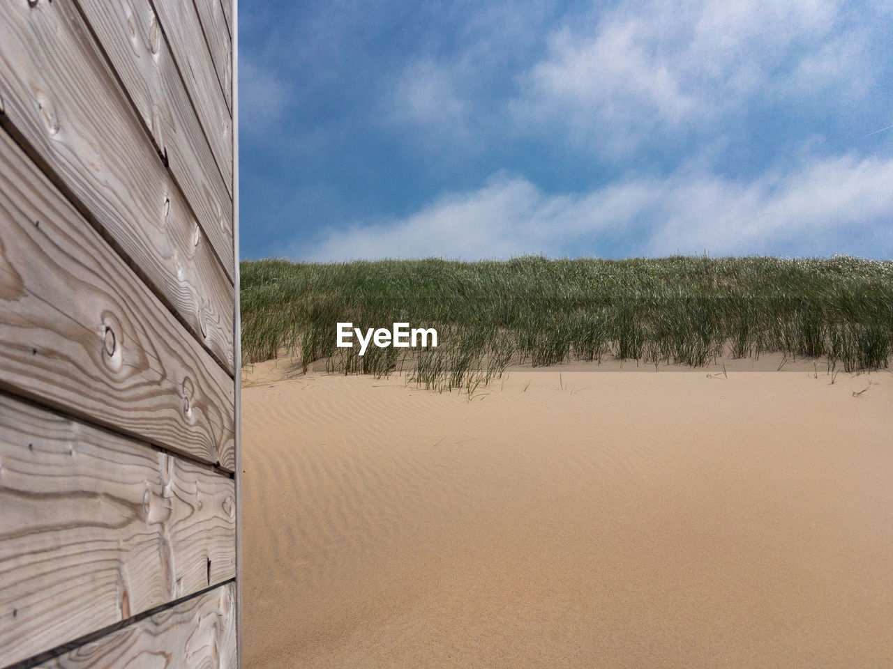 Summertime picture with gray patina wood in front of sand dunes and blue sky