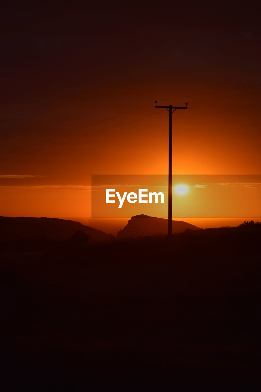 Electricity pylon on field against orange sky