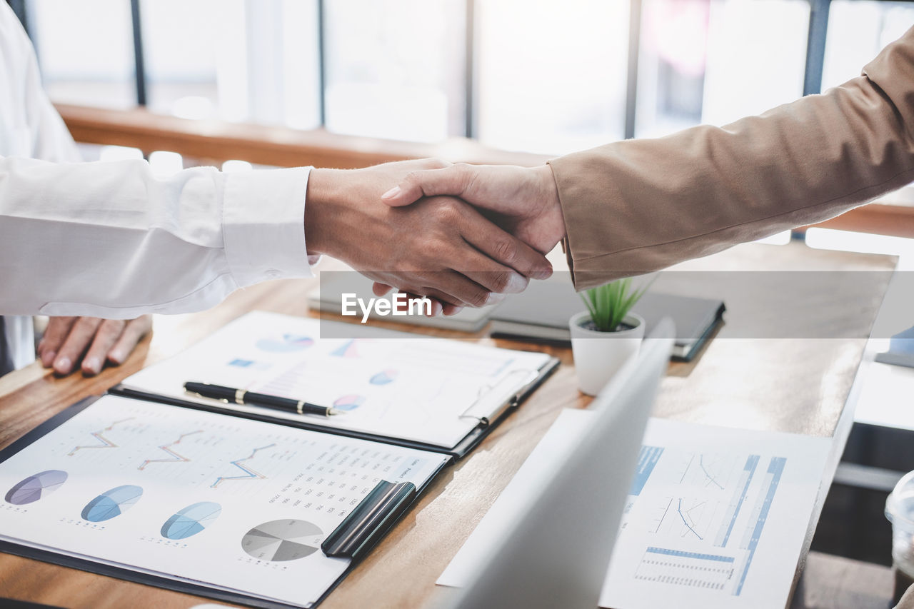 Midsection of businessmen shaking hands at desk in office