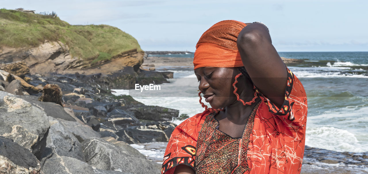 African woman with orange dress on the cliffs by the sea in sekondi-takoradi ghana west africa