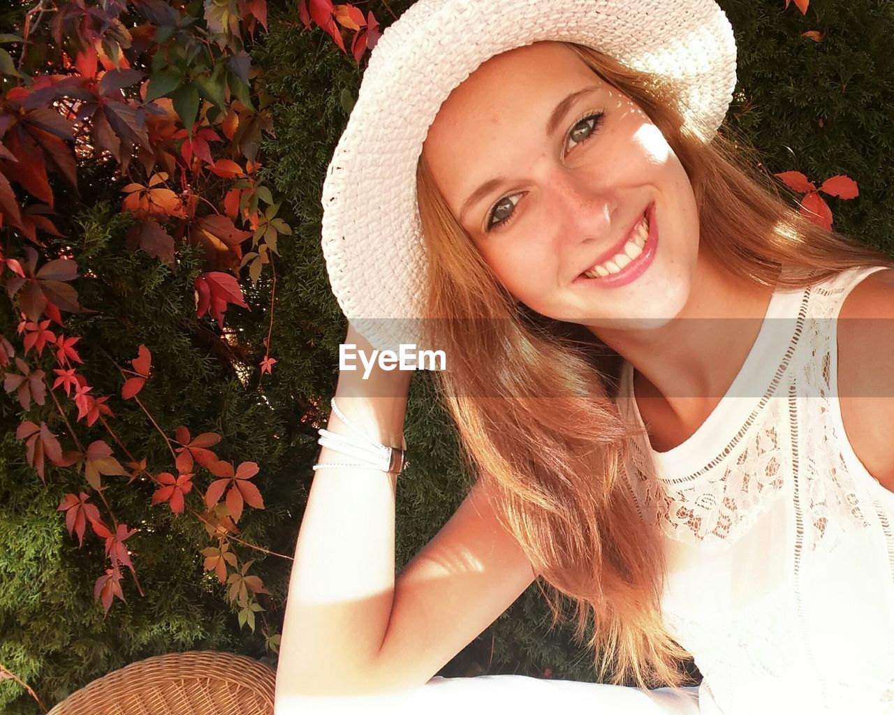 Portrait of beautiful woman wearing hat sitting by plants at park on sunny day