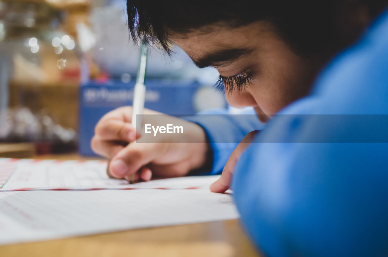 Close-up of boy writing on paper at table