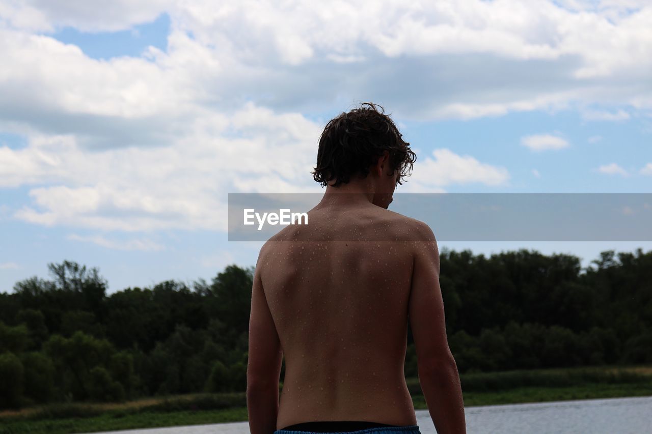 Rear view of shirtless boy standing against sky