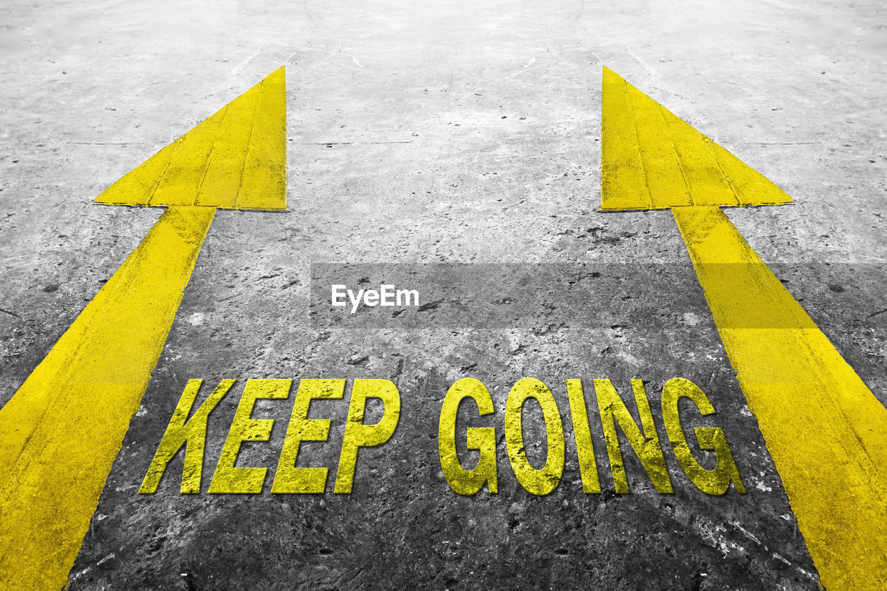 High angle view of keep going text amidst yellow arrow symbols on road