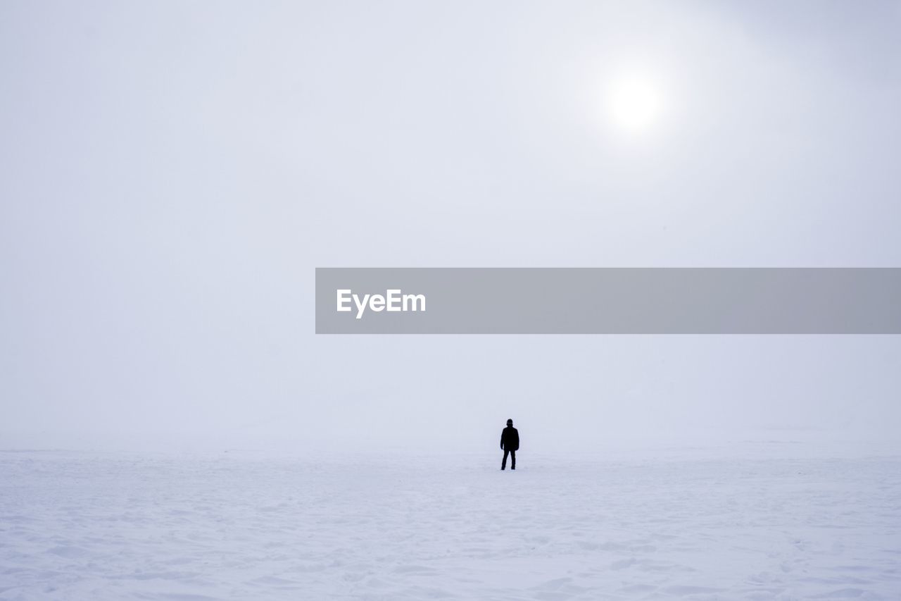 Distant view of silhouette person standing on snow covered field