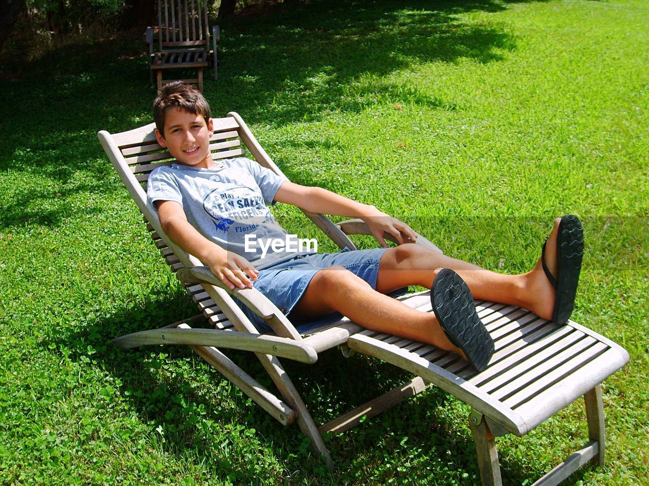 Full length portrait of boy relaxing on lounge chair at lawn during sunny day