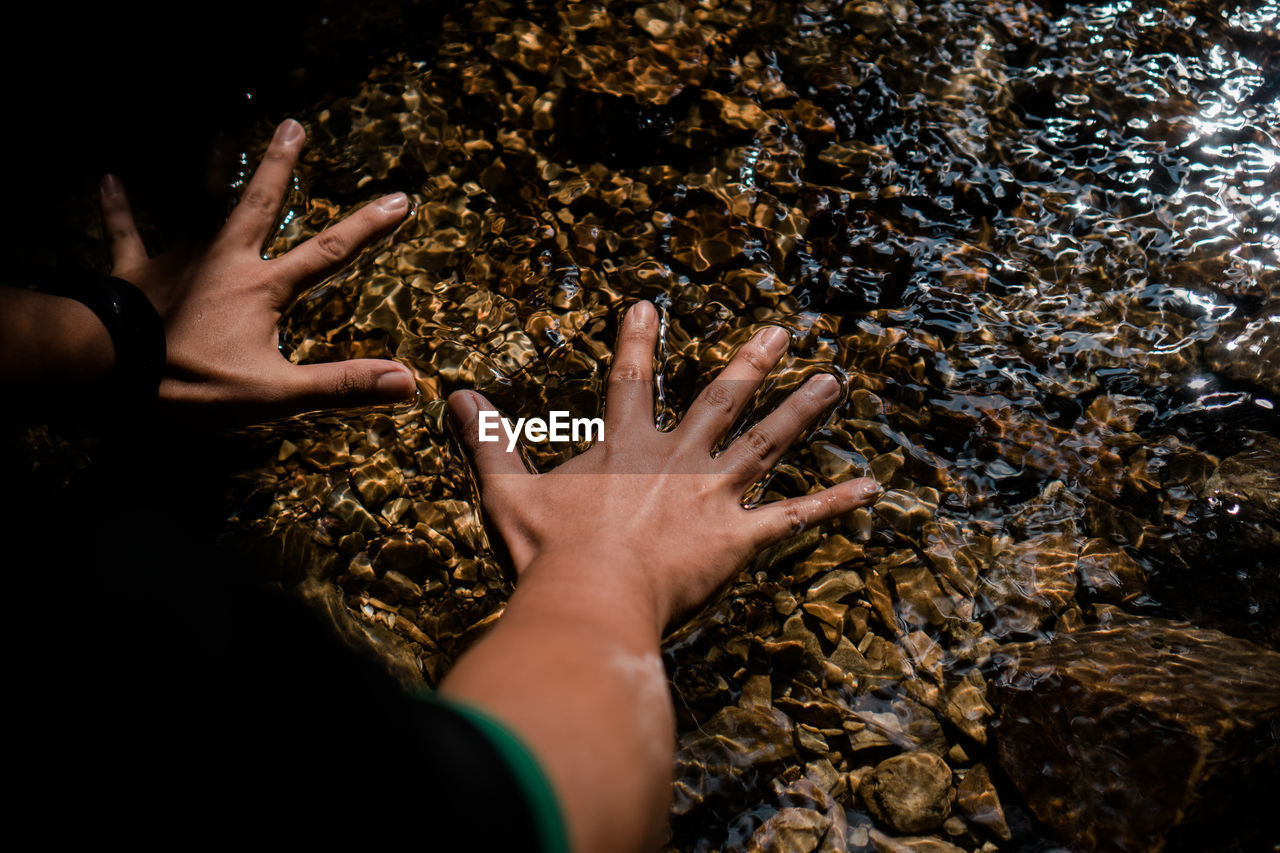 High angle view of hand on rock in shallow water