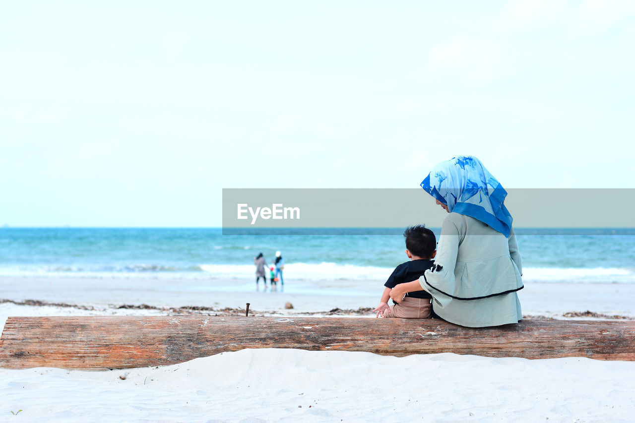 Rear view of mother with baby on beach against sky