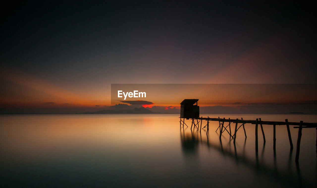 Silhouette of jetty over river at dusk