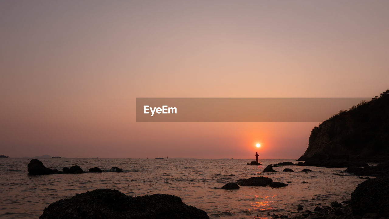 Silhouette fishing man standing on the rock inn the sea and the sunlight background at twilight 