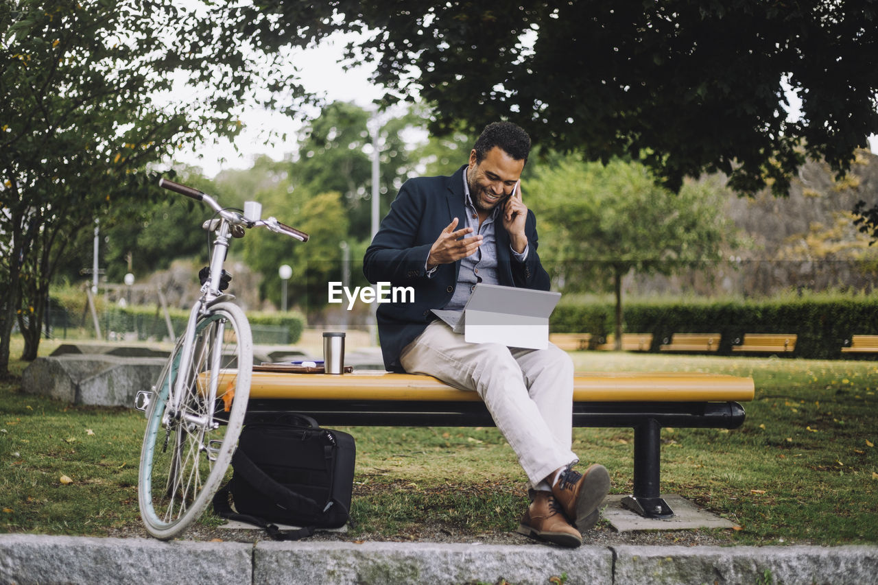 Full length of male freelancer talking on smart phone while sitting in park