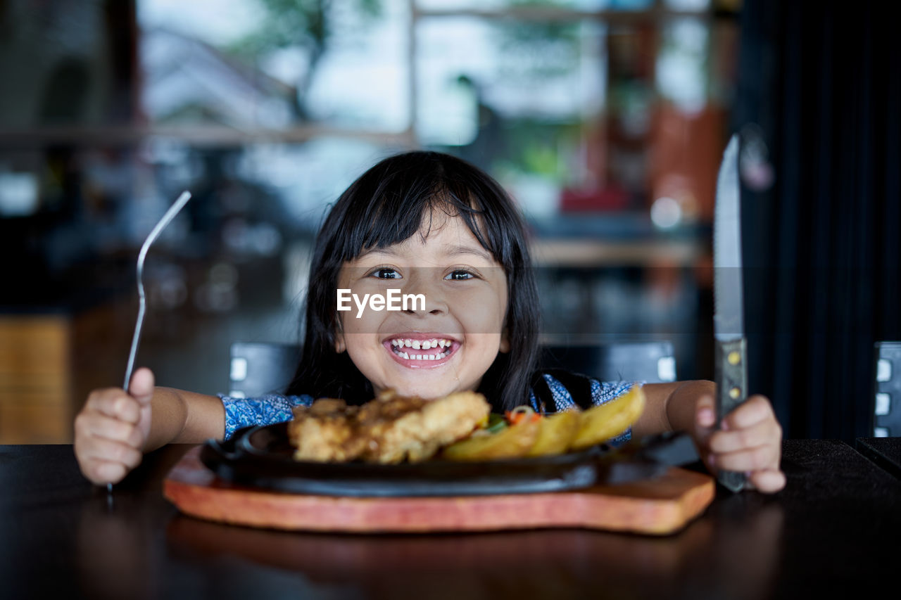 Close-up portrait of smiling girl with food on table in restaurant