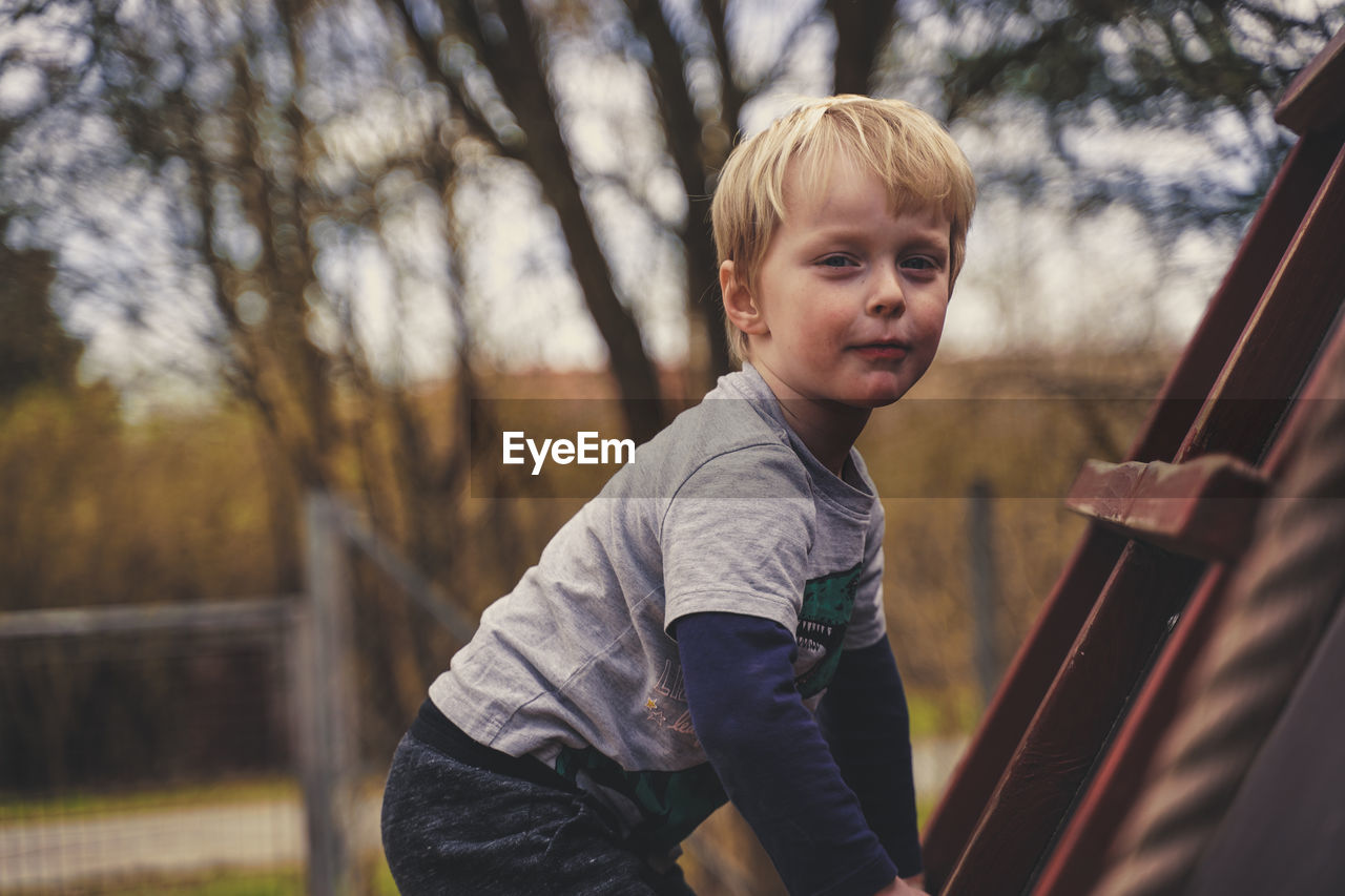 Side view portrait of cute boy climbing on ladder outdoors