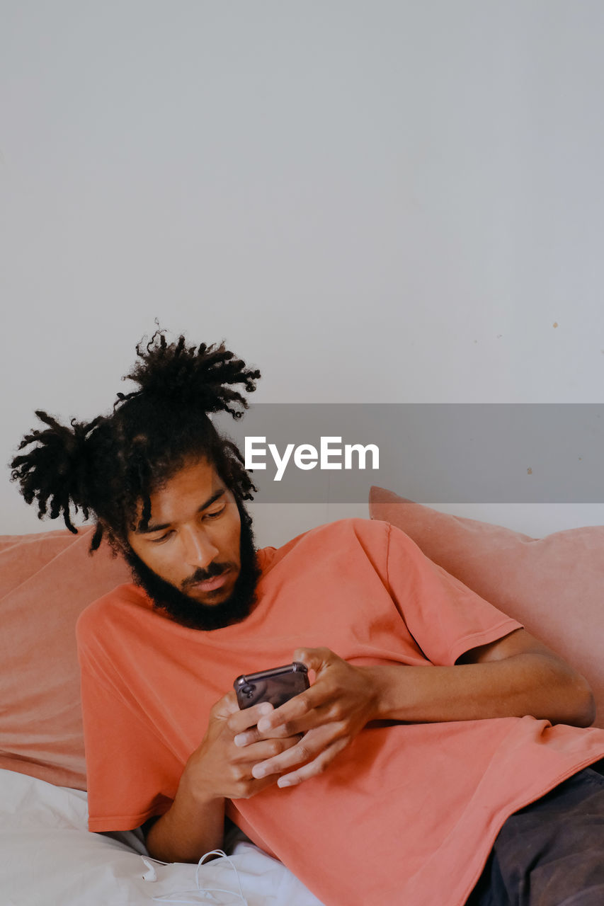 Young man using mobile phone while lying on bed