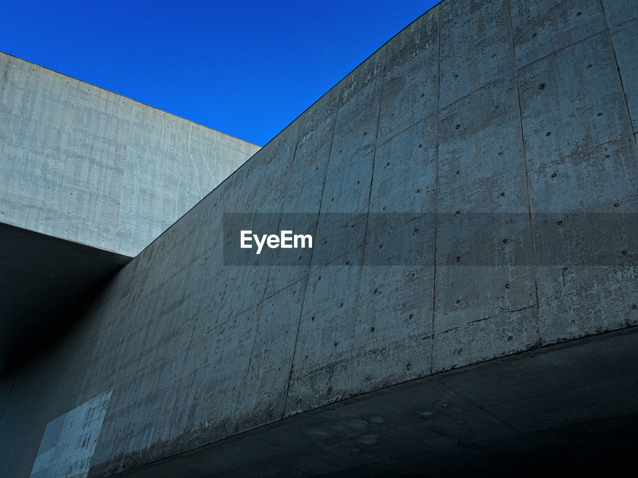 Low angle view of concrete wall against clear blue sky