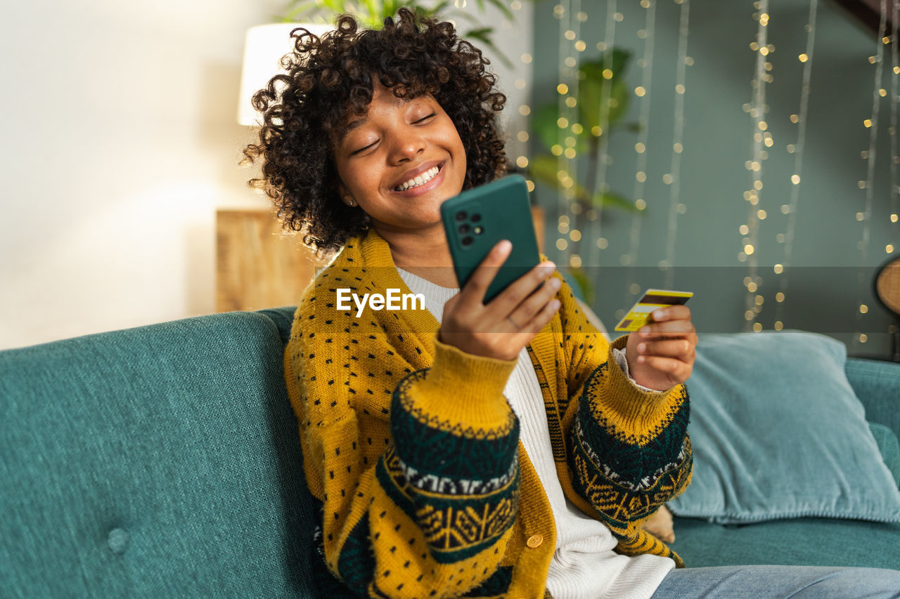 young woman using mobile phone while sitting on sofa at home