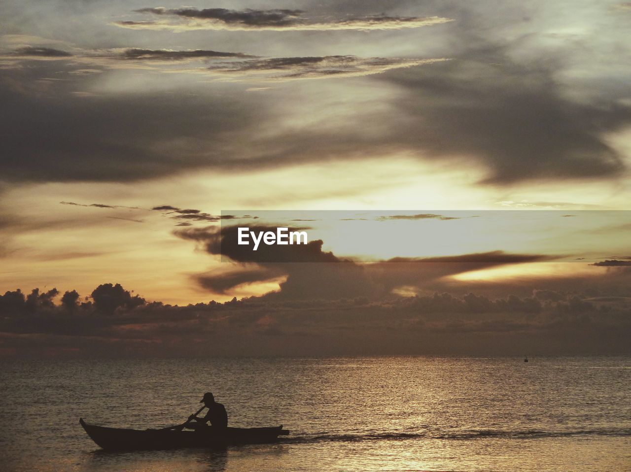 Silhouette man boating in sea against cloudy sky