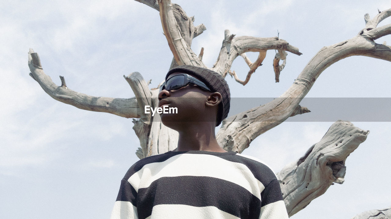 Low angle view of man against sky and dry tree 