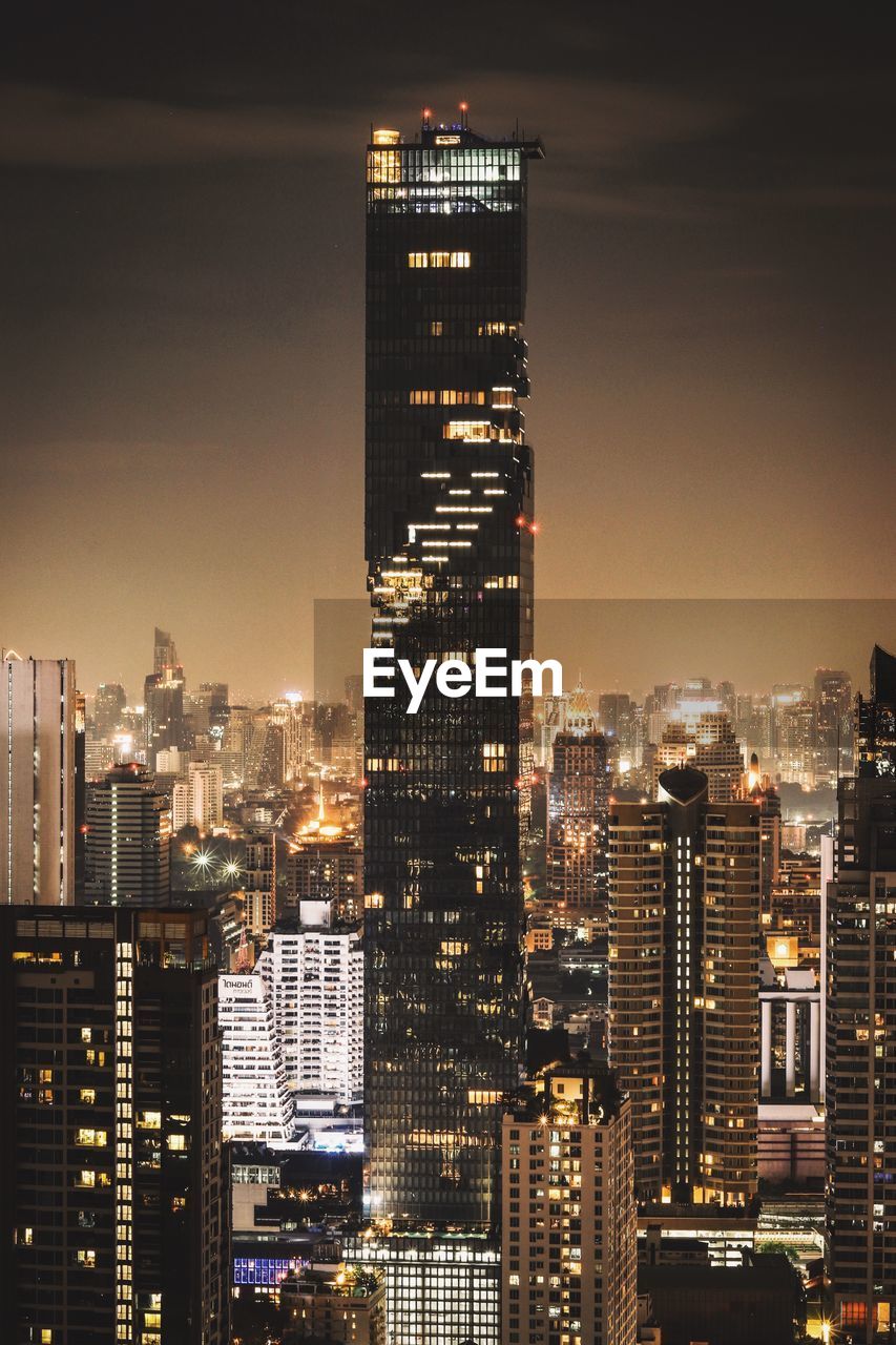 Illuminated modern buildings in city against sky at night