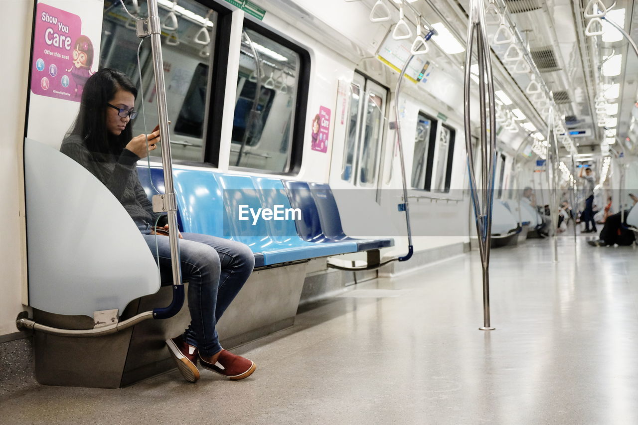 Full length of woman using mobile phone while sitting in subway train
