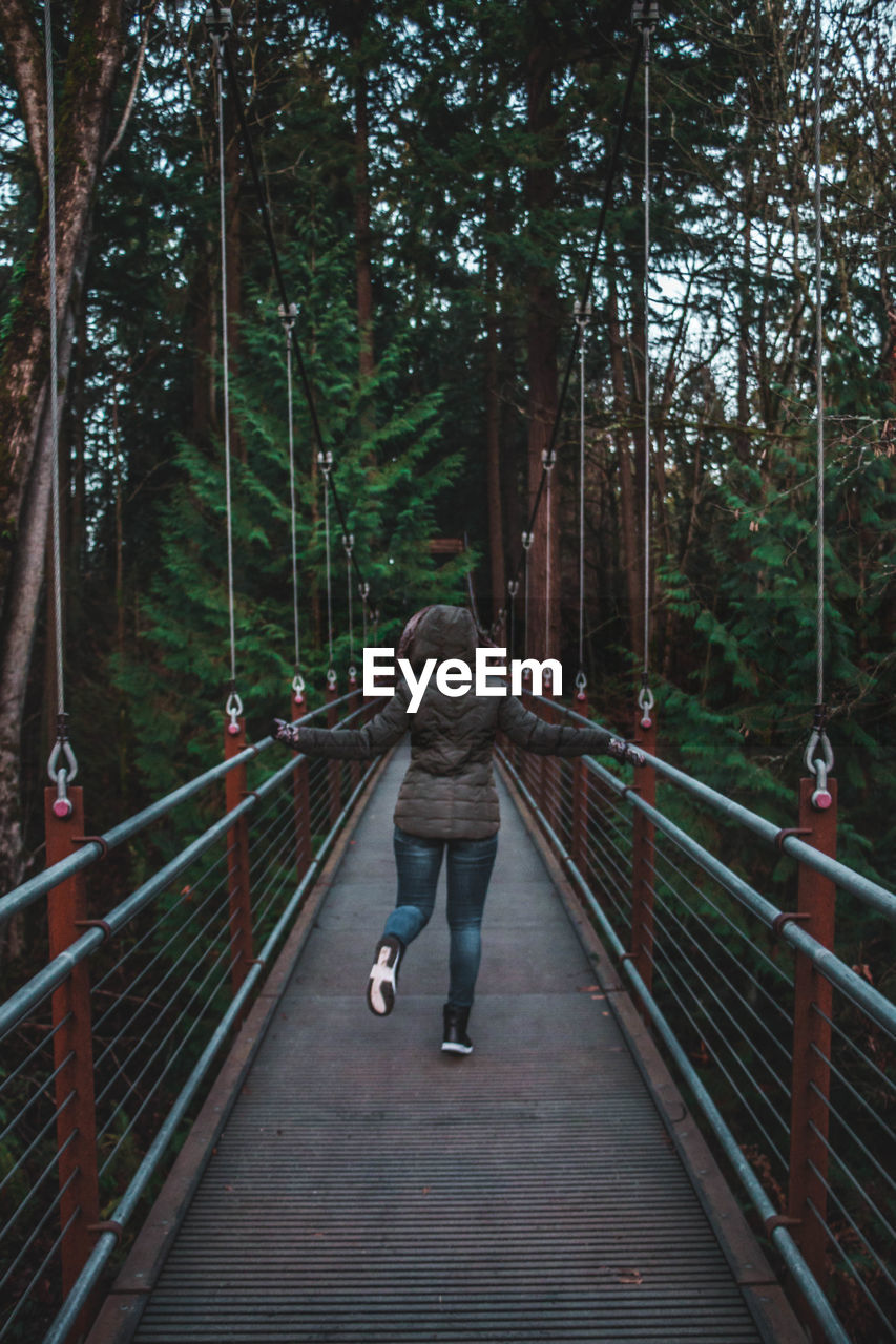 Rear view of woman standing on footbridge in forest