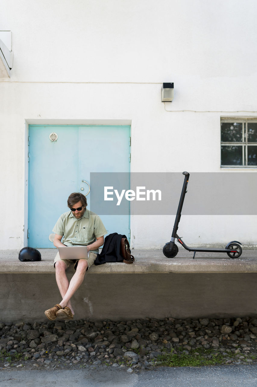 Man with electric scooter using laptop outdoors