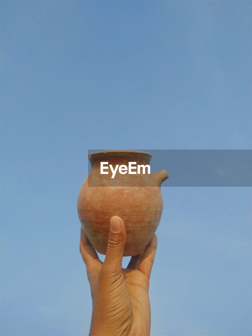 HAND HOLDING ICE CREAM AGAINST BLUE SKY