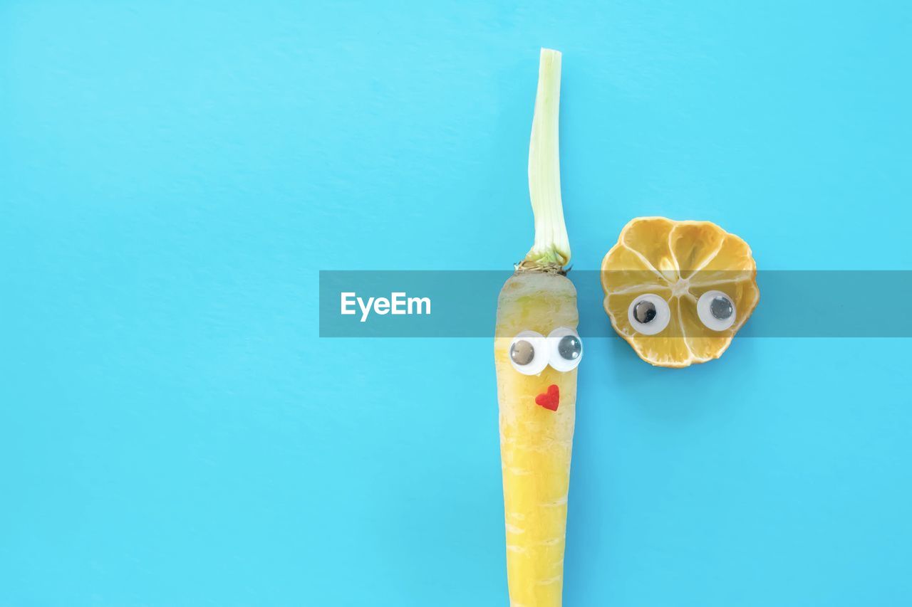 Close-up of carrot and lemon slice with big eyes against blue background