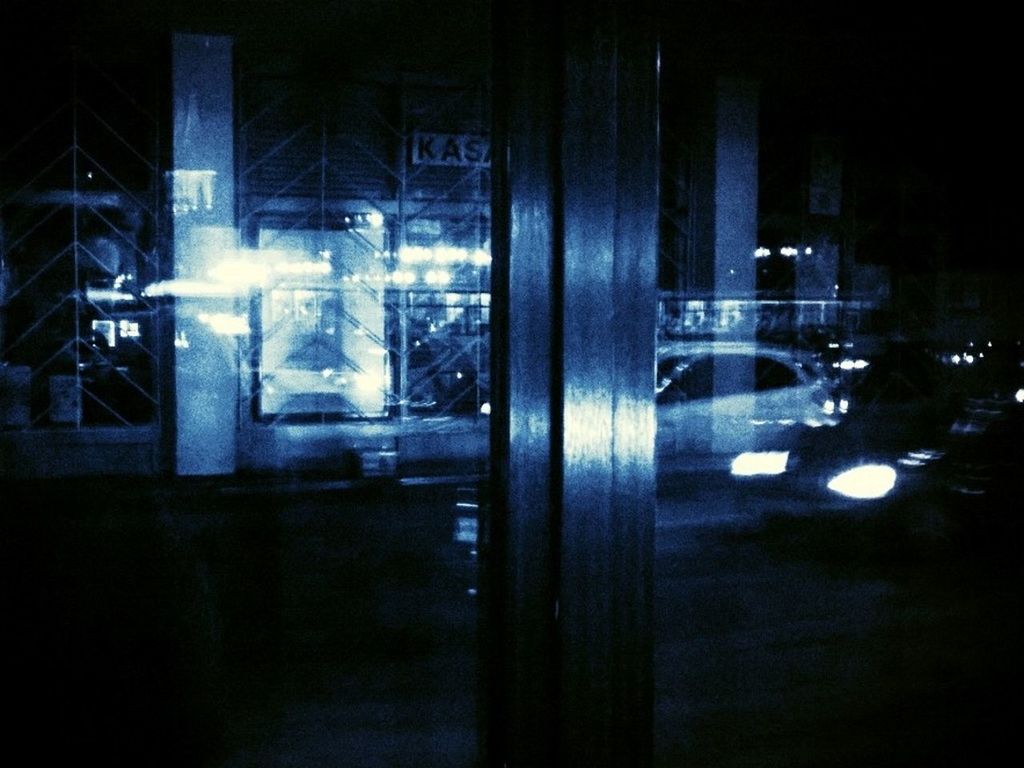 Illuminated cars on street seen glass door at night
