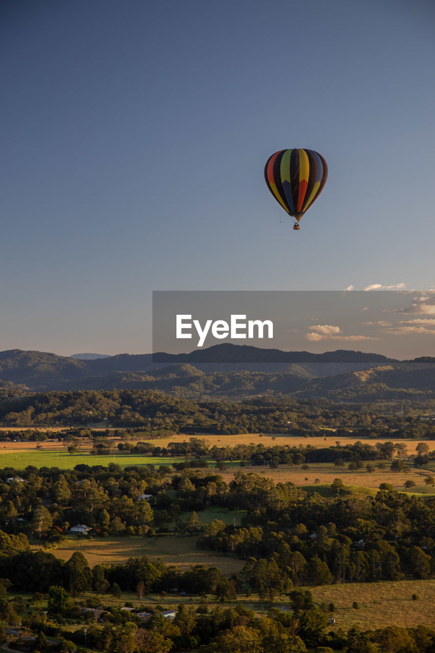 Hot air balloon flying over landscape against clear sky