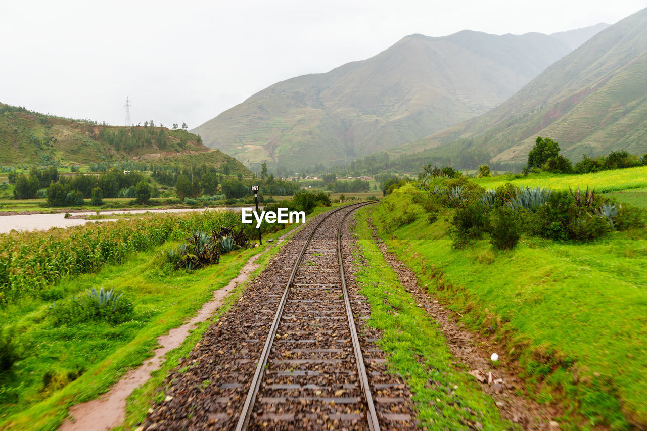 Empty railroad track amidst grassy field leading towards mountains