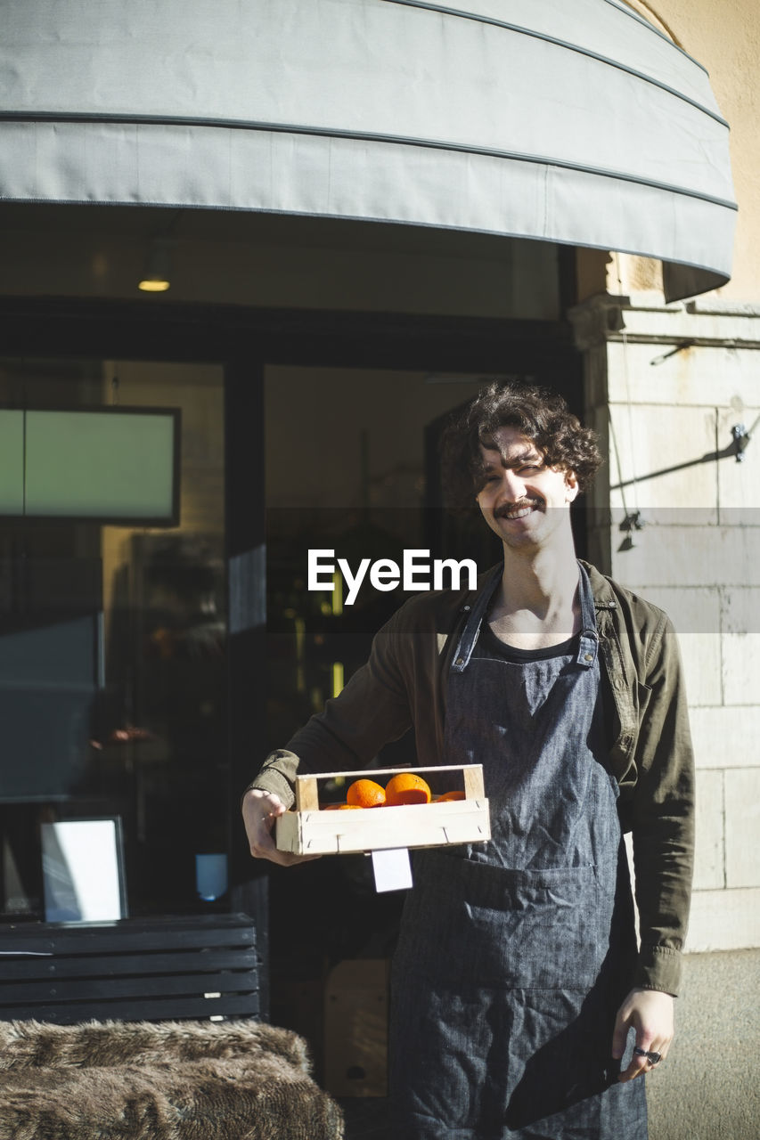 Smiling male entrepreneur with food box standing outside store