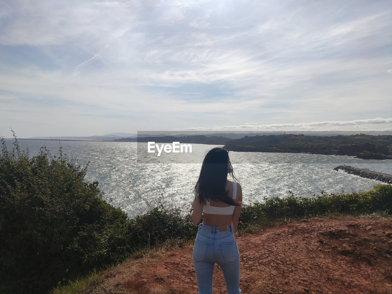 one person, rear view, sky, water, sea, nature, women, leisure activity, cloud, beauty in nature, standing, horizon, casual clothing, land, adult, scenics - nature, lifestyles, tranquility, coast, day, beach, sunlight, tranquil scene, long hair, young adult, vacation, shore, hairstyle, trip, non-urban scene, outdoors, holiday, ocean, environment, full length, three quarter length, morning, plant, idyllic, solitude, horizon over water, remote, landscape, hill, blue, person