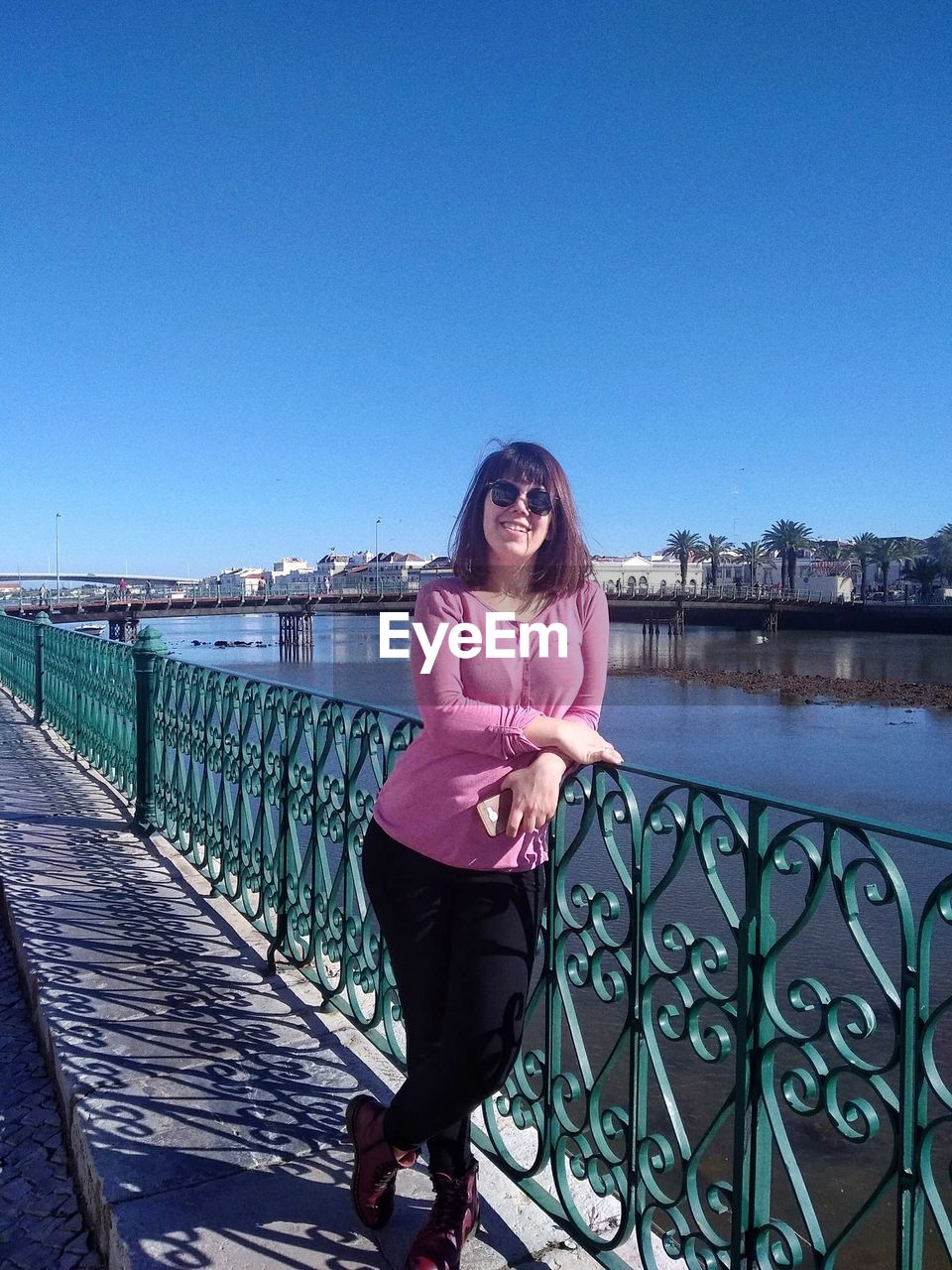 Woman standing by railing against clear blue sky