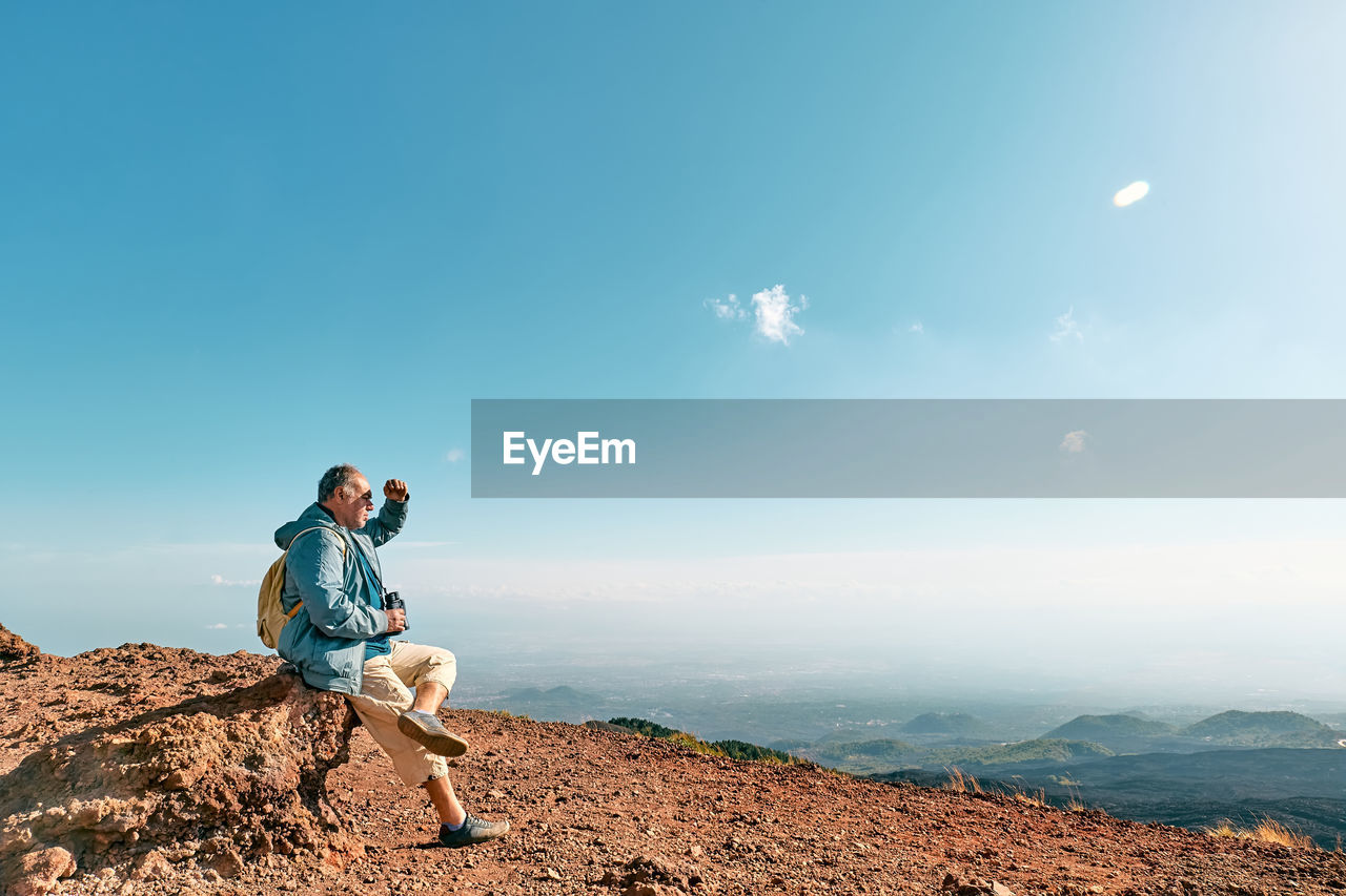 Rear view of man looking through binoculars at panoramic view of colorful summits of volcano etna.