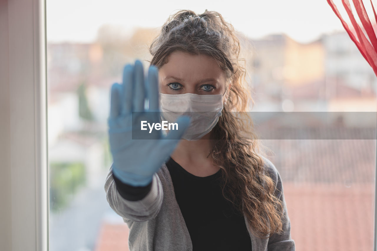 Young woman is doing stop gesture sign,she is wearing surgical mask and gloves