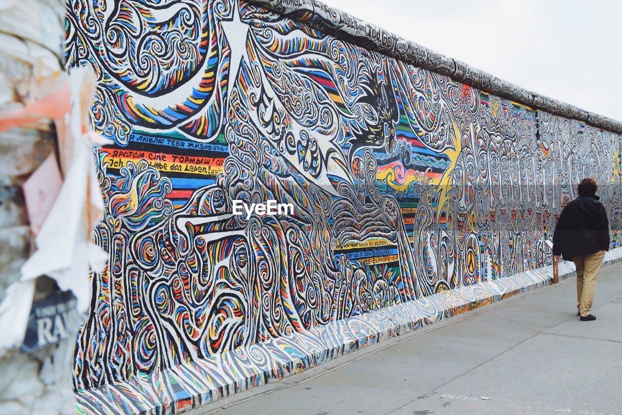 FULL LENGTH REAR VIEW OF WOMAN WALKING ON MULTI COLORED WALL