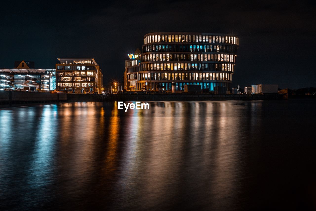 ILLUMINATED CITY BY SEA AGAINST SKY