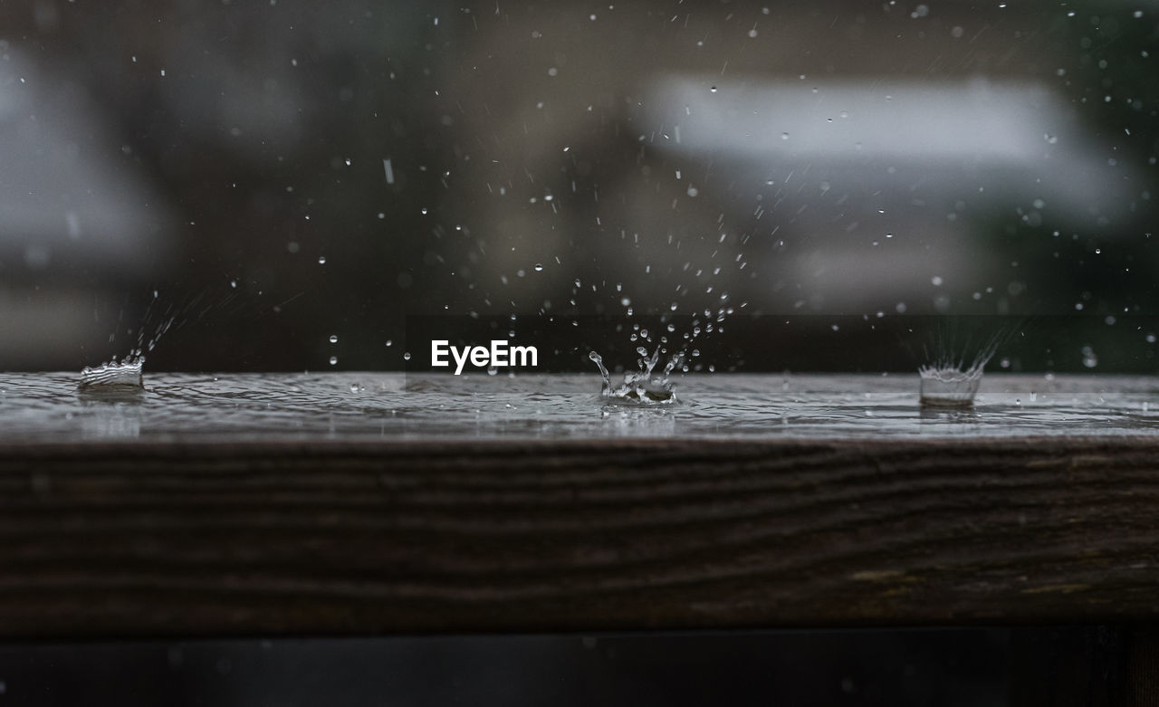 Close up of raindrops hitting a wooden railing with a splash.